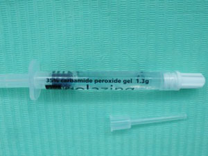 Close up of a plastic syringe of carbamide peroxide tooth whitening gel against a green background