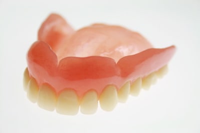 An upper full denture on a glass surface with light coming from underneath