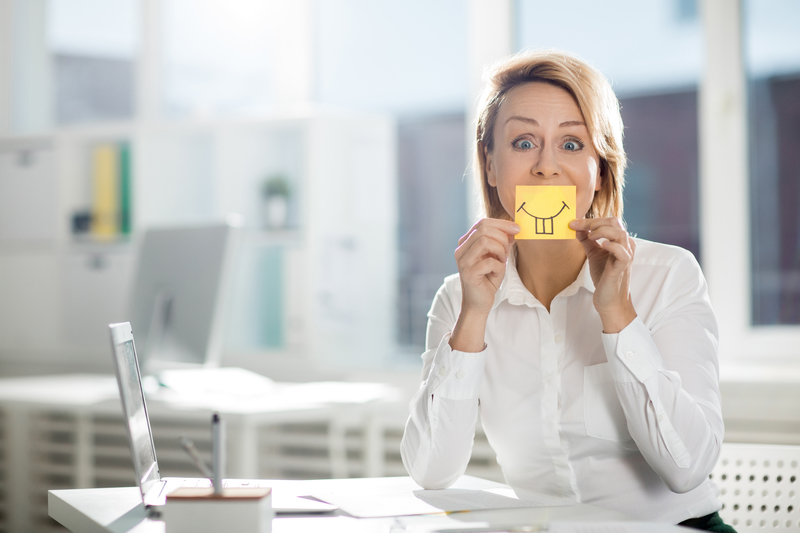 A lady in a white blouse holding a yellow post-it note over her mouth.