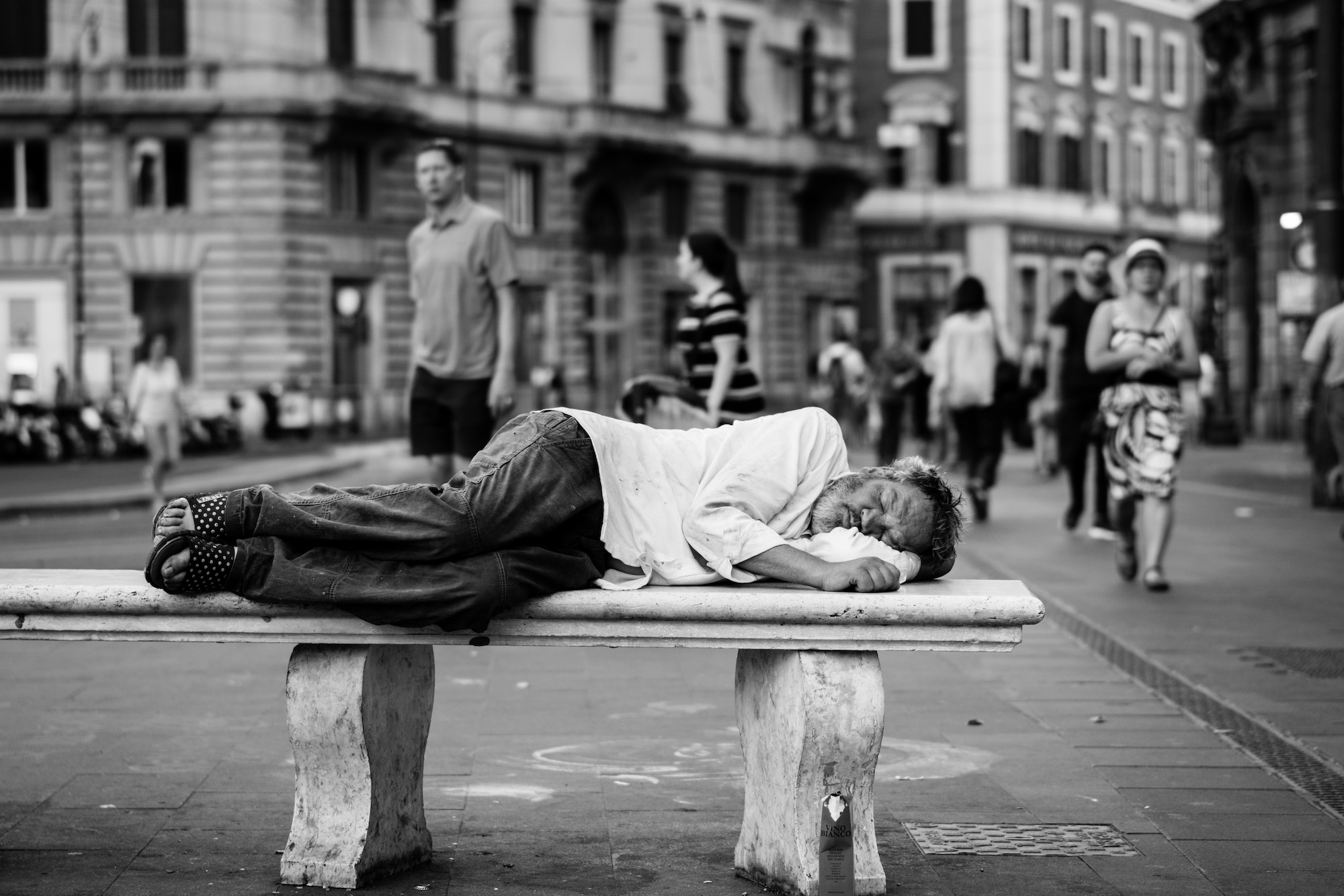 A man in a white shirt sleeping on a public bench