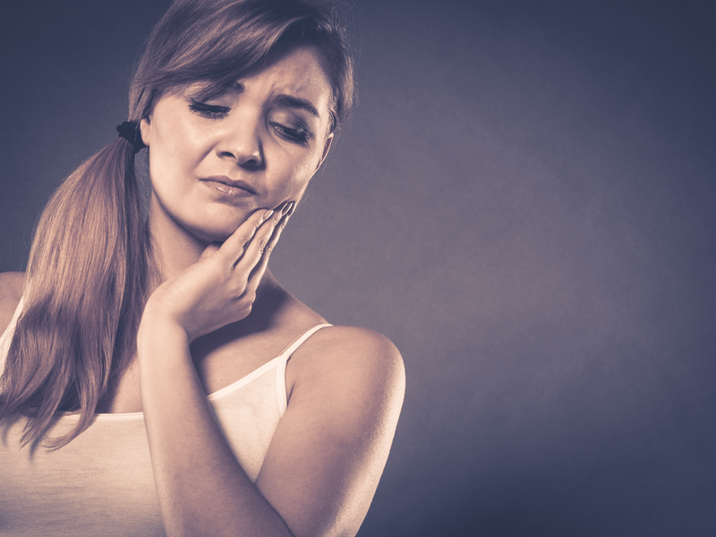 A woman with her hair tied to one side wearing a white top, holding her left hand to her cheek