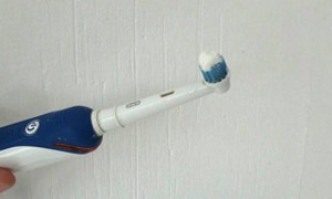 An electric toothbrush being held by a man's hand, next to a white wall